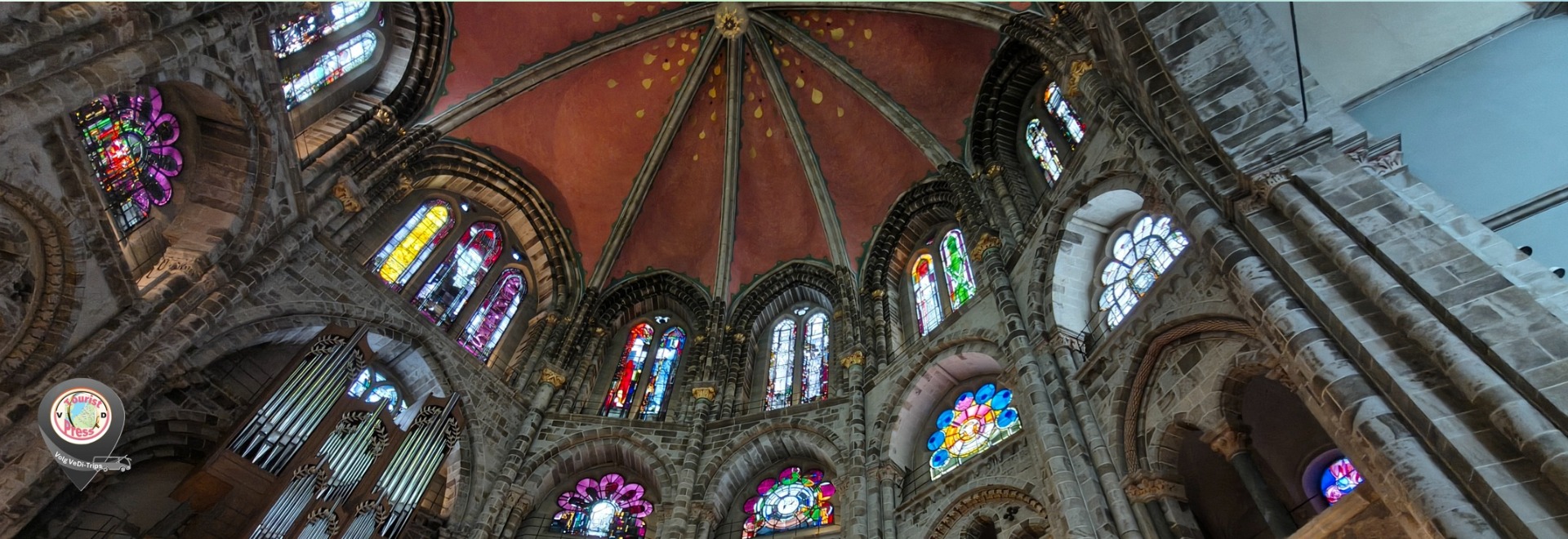 Binnenaanzicht van een gotische kerk met hoge gewelven, glas-in-loodramen en kleurrijke mozaïeken.