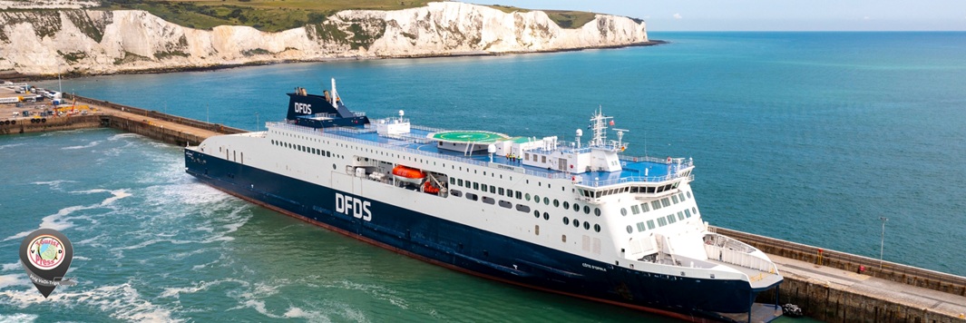Wit en blauw DFDS-schip ligt aan kade in turquoise zee, met krijtrotsen langs de kust.