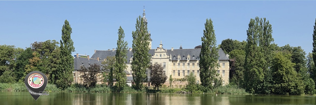 Rivier met weerspiegeling van een kloostercomplex, omringd door hoge bomen en blauwe lucht.