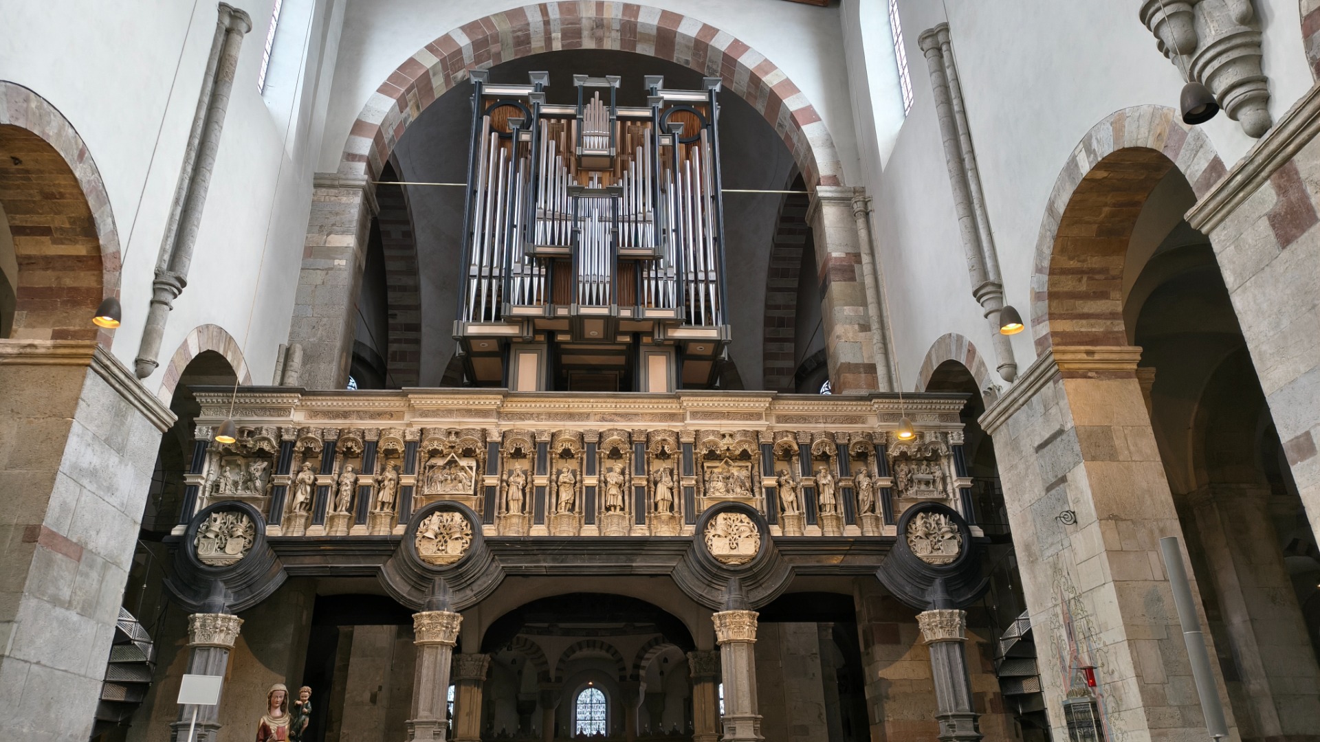 Orgelpijpen en barokke balustrade in een hoge stenen kerk, met bogen, zuilen en boogvensters.