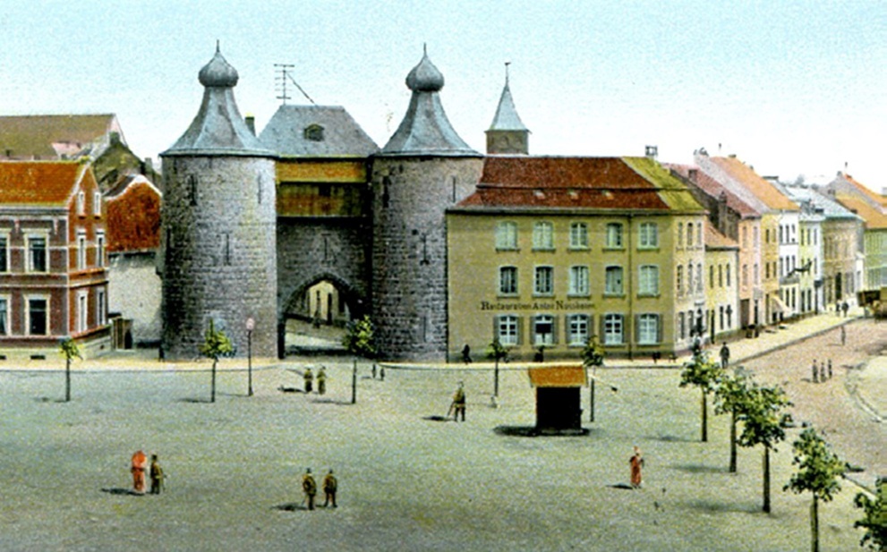 Historisch kasteel met ronde torens en poort, omringd door pleinen en rij huizen onder blauwe lucht.