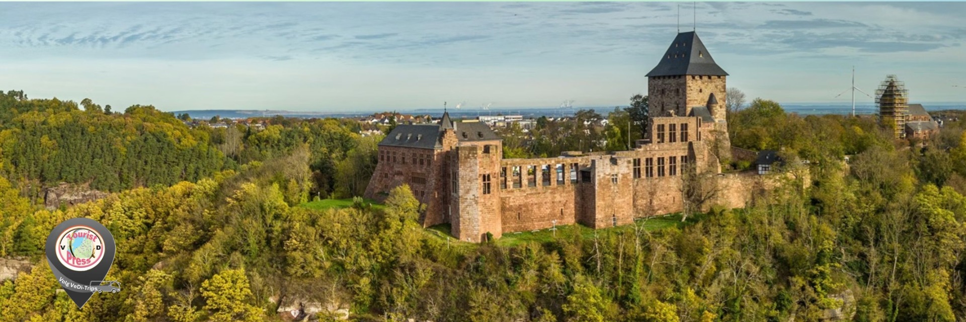 Historisch kasteel met hoge toren omringd door groene bomen, gezien vanuit de lucht bij helder daglicht.