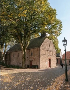 Boterkerkje in Oirschot: Bakstenen gebouw met rieten dak, bomen met herfstbladeren en een straatlantaarn langs een pad.