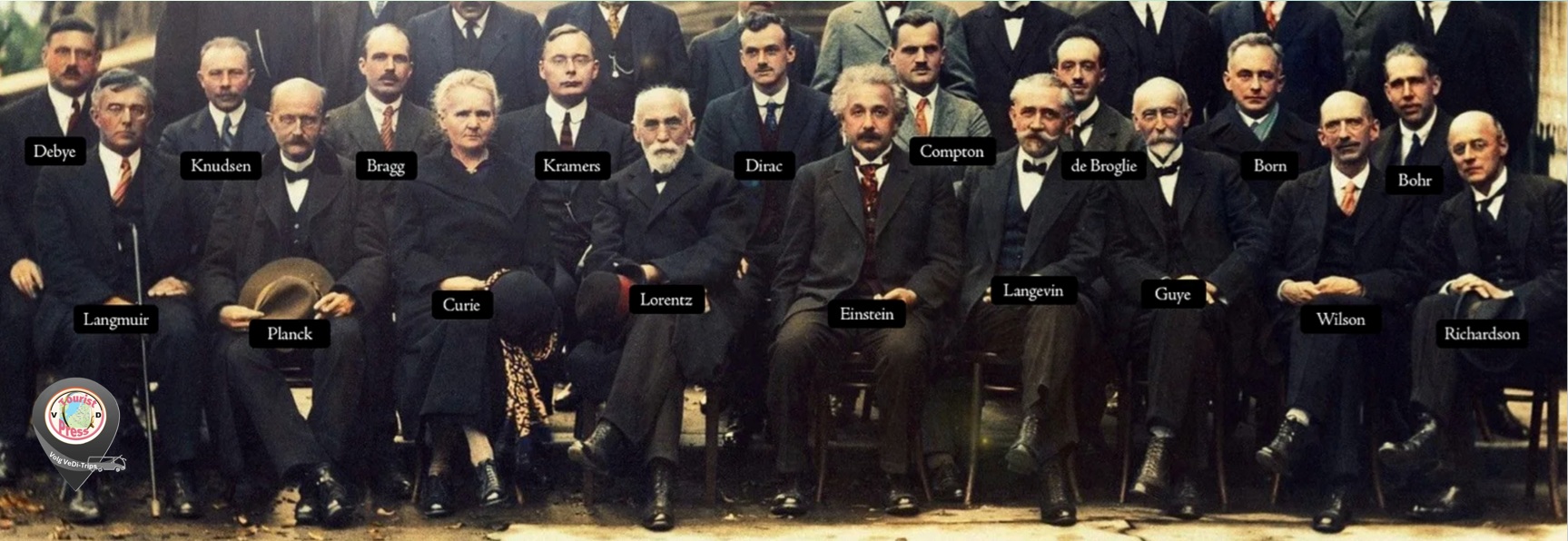 Groepsfoto van wetenschappers in formele pakken, met naamplaatjes zoals Einstein, Curie en Dirac.
