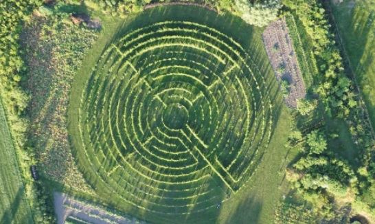 Luchtfoto van een groen doolhof met concentrische ringen en een pad in het midden.