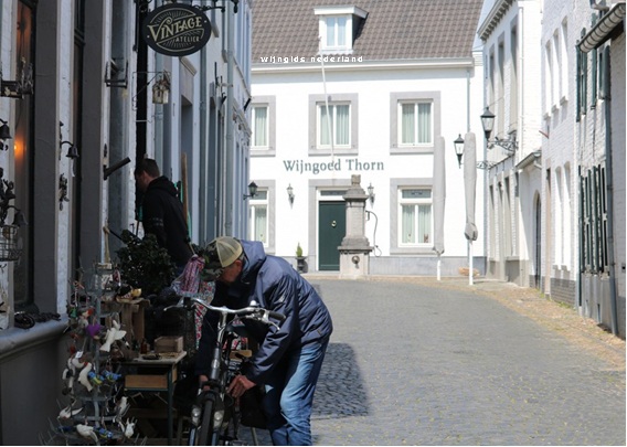 Man loopt langs smalle steeg met winkeldecoraties en fietsen, voor gevel met bord “Vintage Atelier”.